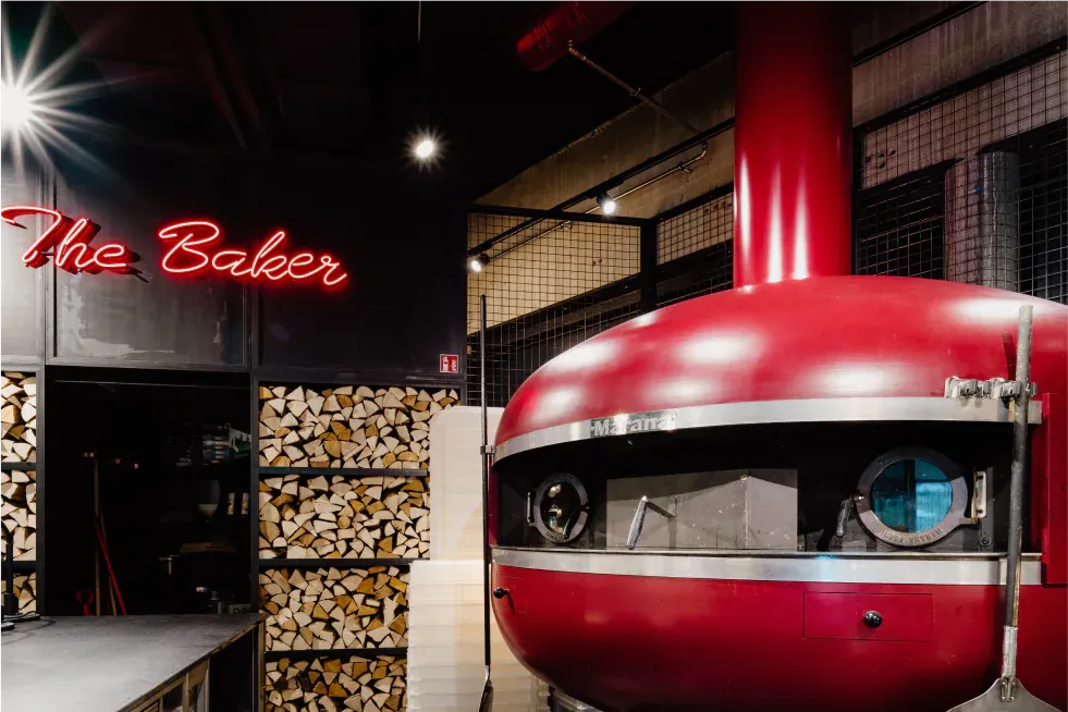 Červená pec na dřevo pod neonovým nápisem „The Baker“
